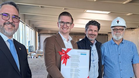 Neustadt an der Weinstraße, 23. April 2026. Ein bedeutender Baufortschritt ist erreicht: Mit einem feierlichen Richtfest haben wir den Rohbau unserer neuen Mercedes-Benz Autowelt in der Bertha-Benz-Straße abgeschlossen. Gemeinsam mit rund 100 Gästen, darunter Mitarbeitende, Projektpartner, Handwerker sowie Vertreter aus Politik und Presse, wurde dieser Meilenstein gebührend gefeiert. Auch Neustadts Bürgermeister Marc Weigel nahm an der Veranstaltung teil.
Die Feierlichkeiten fanden in der künftigen Ausstellungshalle statt und wurden von unserem CEO Thomas Kestenholz eröffnet. Weitere Einblicke in das Projekt gaben Holger Krimmel (COO Wirtschaftsraum Pfalz) und Steffen Scheich (Centerleiter Neustadt). Ein besonderer Moment war das Hissen der Richtkrone sowie der traditionelle Richtspruch durch Guido Leuthner (Freyler Industriebau). &nbsp;
Moderner Standort mit Zukunft
Der neue Gebäudekomplex soll bis Ende 2026 fertiggestellt werden und zählt schon jetzt zu den modernsten Autohäusern der Region. Auf rund 6.560 Quadratmetern entstehen Verkaufs-, Service- und Erlebnisbereiche unter einem Dach. Herzstück ist eine lichtdurchflutete Ausstellungshalle mit sieben Metern Höhe, die Raum für die neuesten Pkw- und Van-Modelle von Mercedes-Benz bietet.
Neben modernen Arbeitsplätzen entstehen auch kundenorientierte Bereiche wie ein Café, eine VIP-Lounge und offene Beratungsflächen für ein ganzheitliches Markenerlebnis.
 Effiziente Abläufe und umfassender Service
Hinter den Kulissen sorgt ein durchdachtes Konzept für maximale Effizienz: Werkstatt, Annahme, Fahrzeugauslieferung und Logistik sind optimal miteinander vernetzt. Über 20 Werkstattarbeitsplätze, ein großes Reifenlager, ein integriertes Lackier- und Karosseriezentrum sowie eine eigene Waschanlage gewährleisten umfassende Serviceleistungen.
 Nachhaltigkeit im Fokus
Der Neubau erfüllt den KfW-55-Standard und setzt auf energieeffiziente Lösungen wie eine Luft-/Wasser-Wärmepumpe, Photovoltaik sowie Dachbegrünung.
 Ein Herzensprojekt für die Region
„Der Neubau in Neustadt ist für uns ein echtes Herzensprojekt“, betont CEO Thomas Kestenholz. „Wir schaffen hier eine moderne Erlebniswelt für unsere Kundinnen und Kunden und investieren gleichzeitig in die Zukunft unseres Unternehmens.“
Mit der neuen Autowelt bauen wir unsere Präsenz in der Region weiter aus und setzen ein starkes Zeichen für Innovation, Servicequalität und Kundennähe.